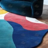 Bold multicolor rug in abstract shape under staircase and blue couch