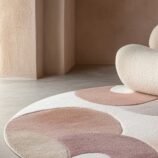 Abstract round wool rug in warm earth tones with modern sculptural chair and neutral interior