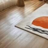 Minimalist Japandi sunrise wool rug with orange sun and black waves on cream background placed in a serene modern living room