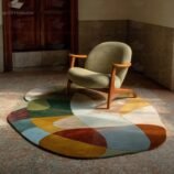 Hand-tufted sculptural abstract wool rug in rich earthy tones under modern chair in sunlight