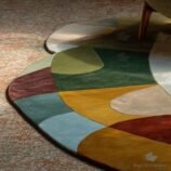 Hand-tufted sculptural abstract wool rug in rich earthy tones under modern chair in sunlight