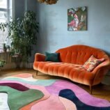 Hand-tufted multicolor wool rug in irregular shape under retro orange sofa in vibrant living room