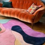 Hand-tufted multicolor wool rug in irregular shape under retro orange sofa in vibrant living room