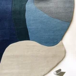 Modern abstract area rug in warm earth tones of orange, blue, and beige, handcrafted for modern interiors.