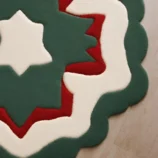 Modern star-shaped rug with green, red, and white layers, handcrafted for festive and elegant interiors.